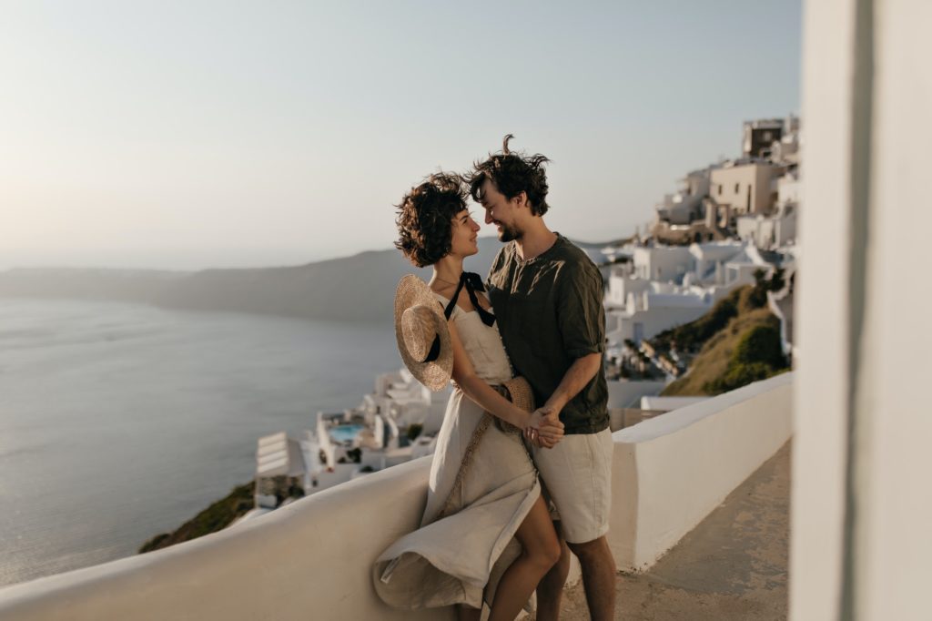 Portrait of couple on background of Greek city. Brunette lady in beige dress and man in stylish out